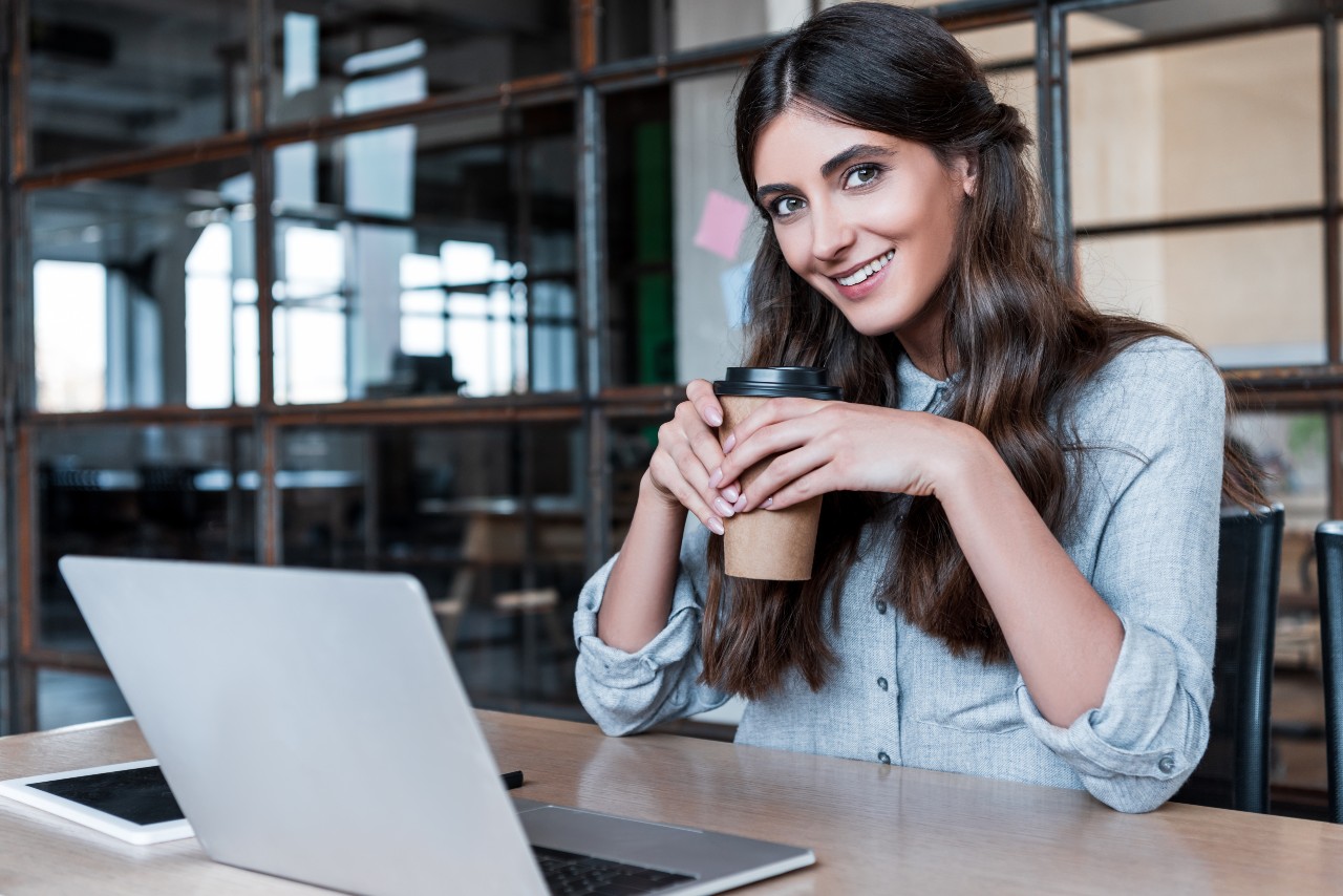 happy young businesswoman holding paper cup and smiling