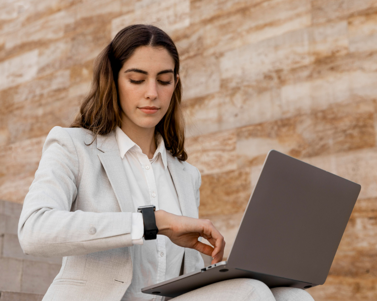 Elegant businesswoman looking at smartwatch and working on laptop outdoors