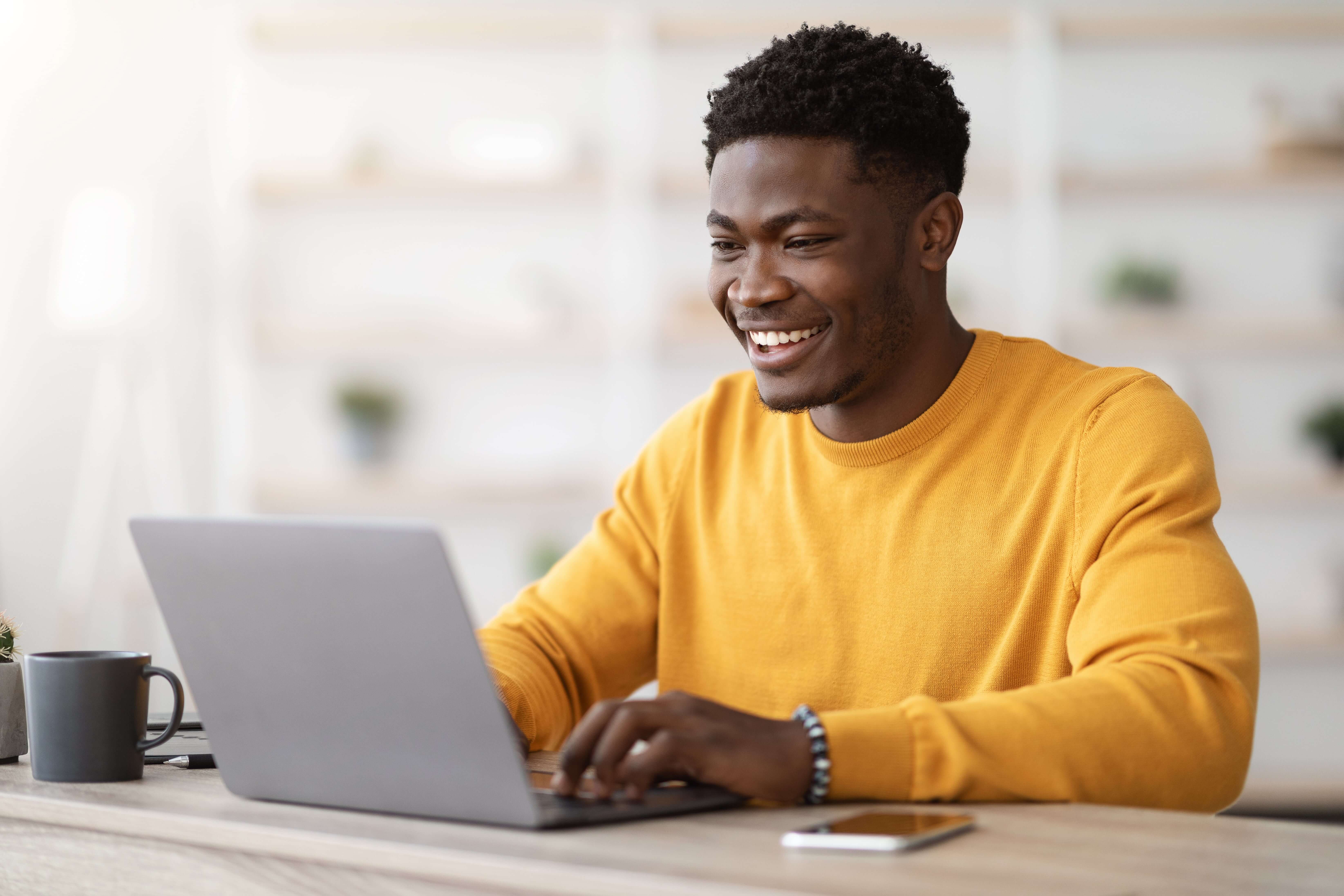 Man in yellow jumper smiling at laptop
