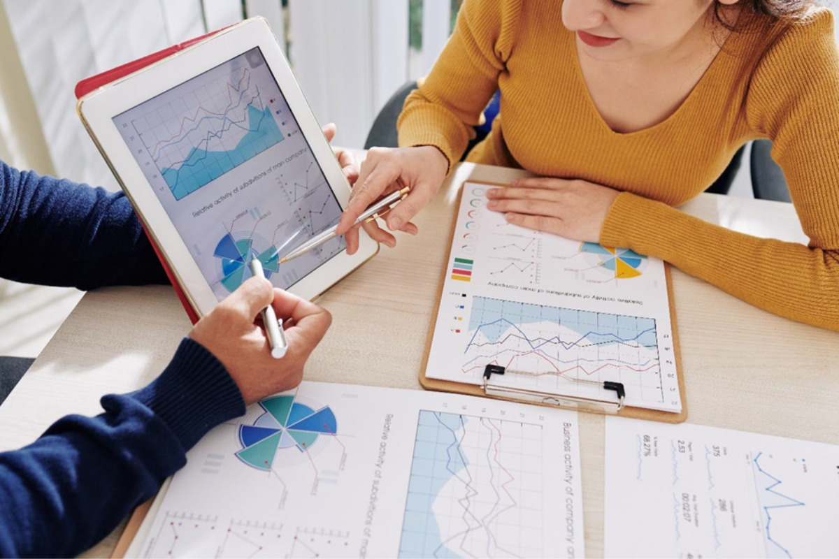 People sitting at desk looking at statistic sheets on clipboard and tablet.